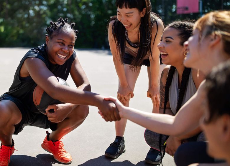 teen girls on outdoor basketball court smiling and shaking hands.