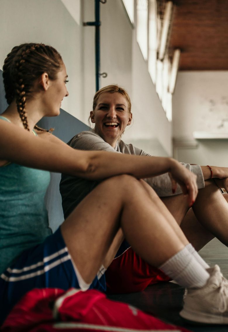 teen girls sitting on gym floor laughing.