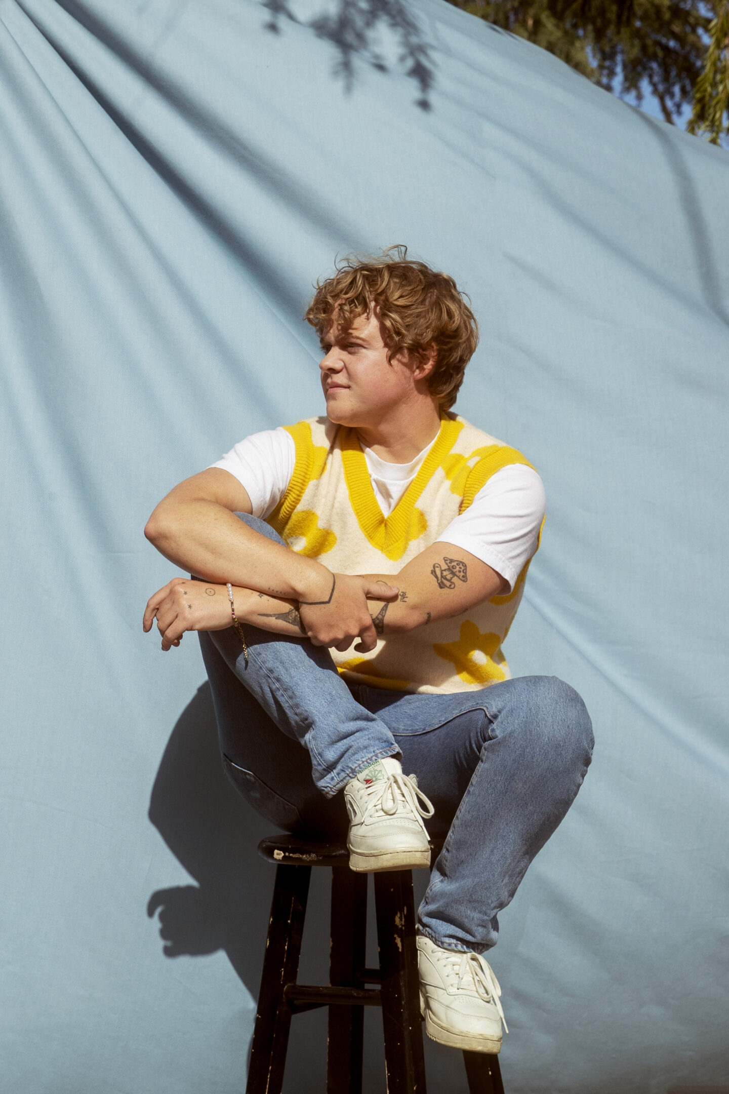 Portrait of a young person with a yellow sweater vest posing against a light blue backdrop