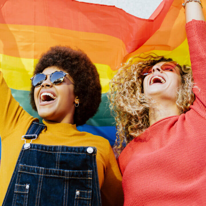 Two people celebrating under a pride flag.
