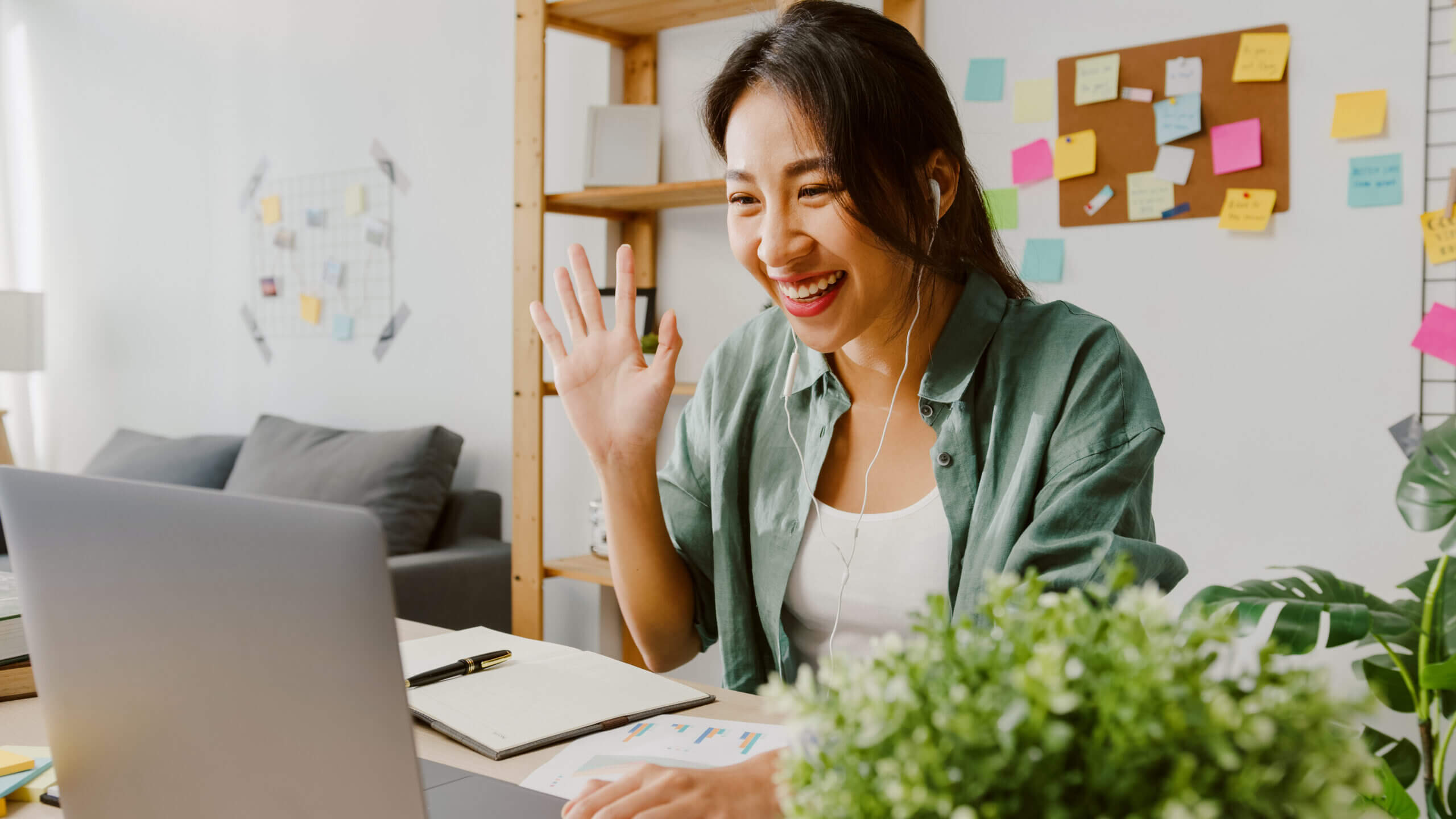 Smiling staff member waving to a coworker over video chat while working from their home office.