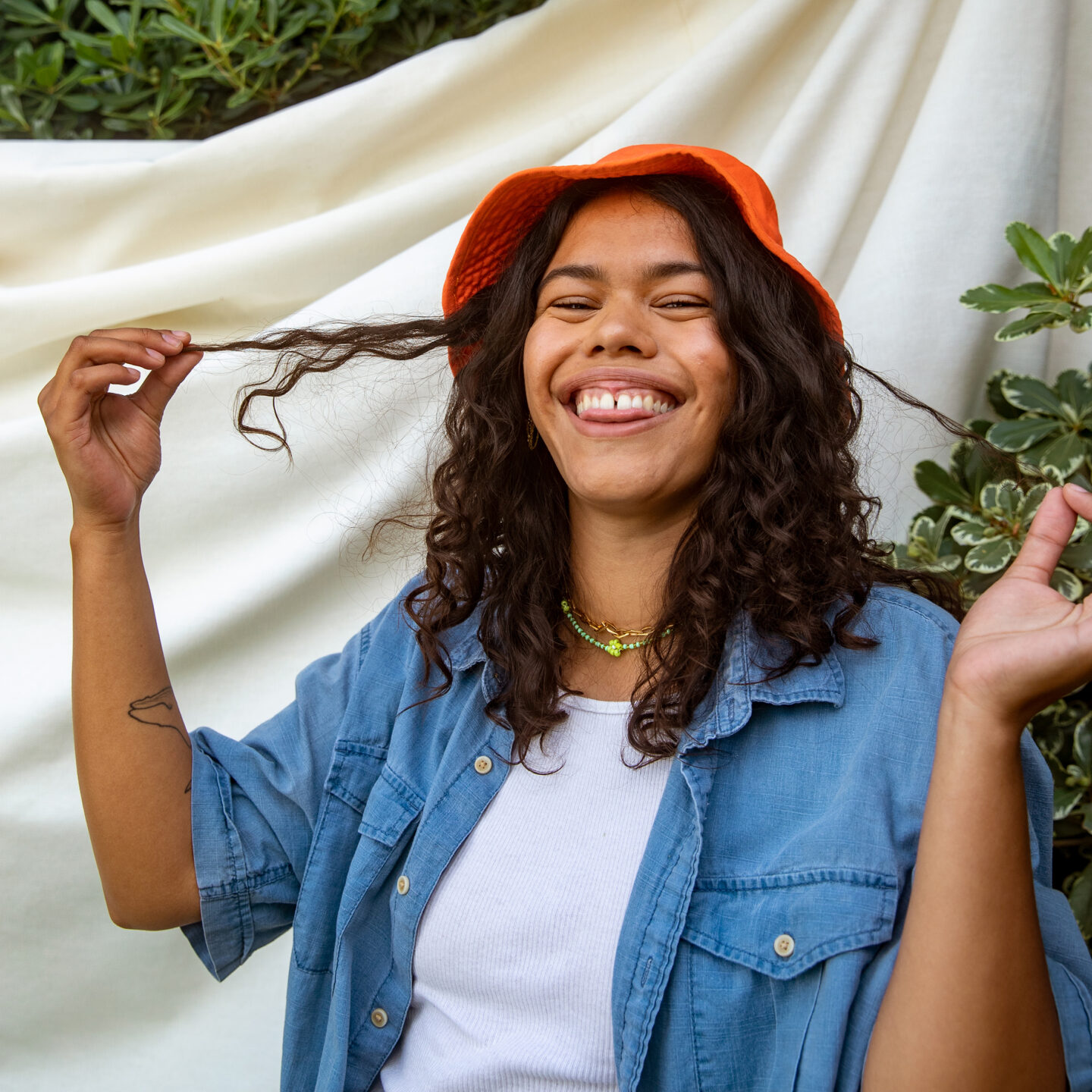 Young person laughing, standing outside in front of a neutral fabric backdrop