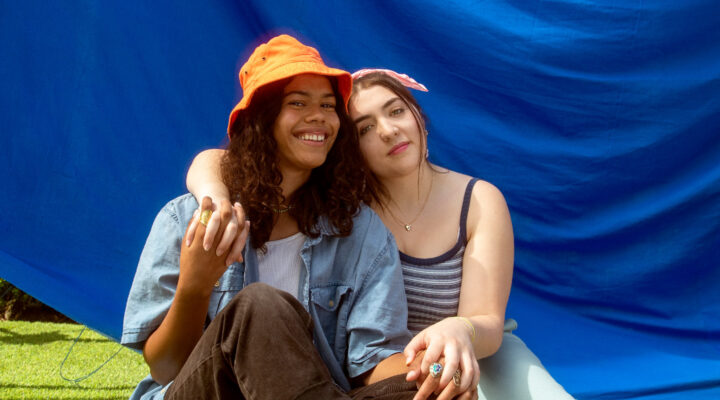 Two young people holding hands and posing against a blue backdrop