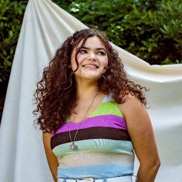 Portrait of a young person in a striped shirt, standing outside in front of a neutral fabric backdrop