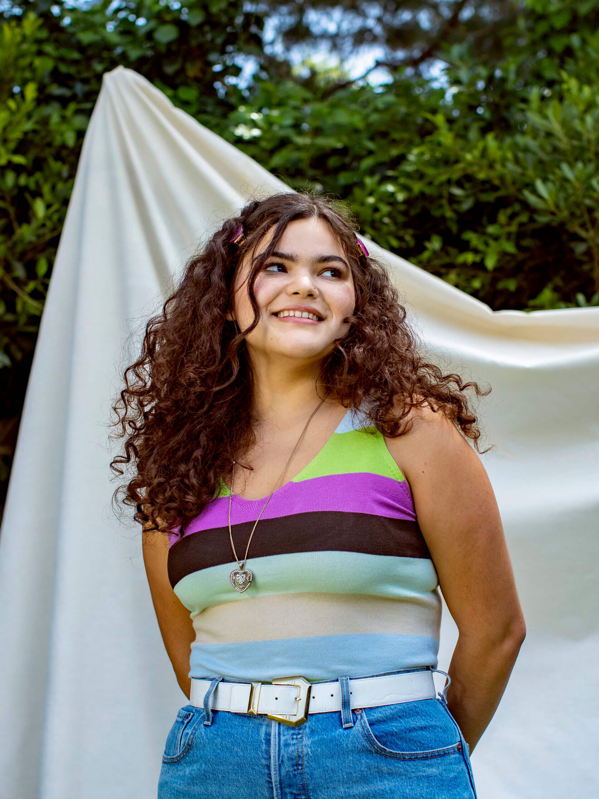 Portrait of a young person in a striped shirt, standing outside in front of a neutral fabric backdrop