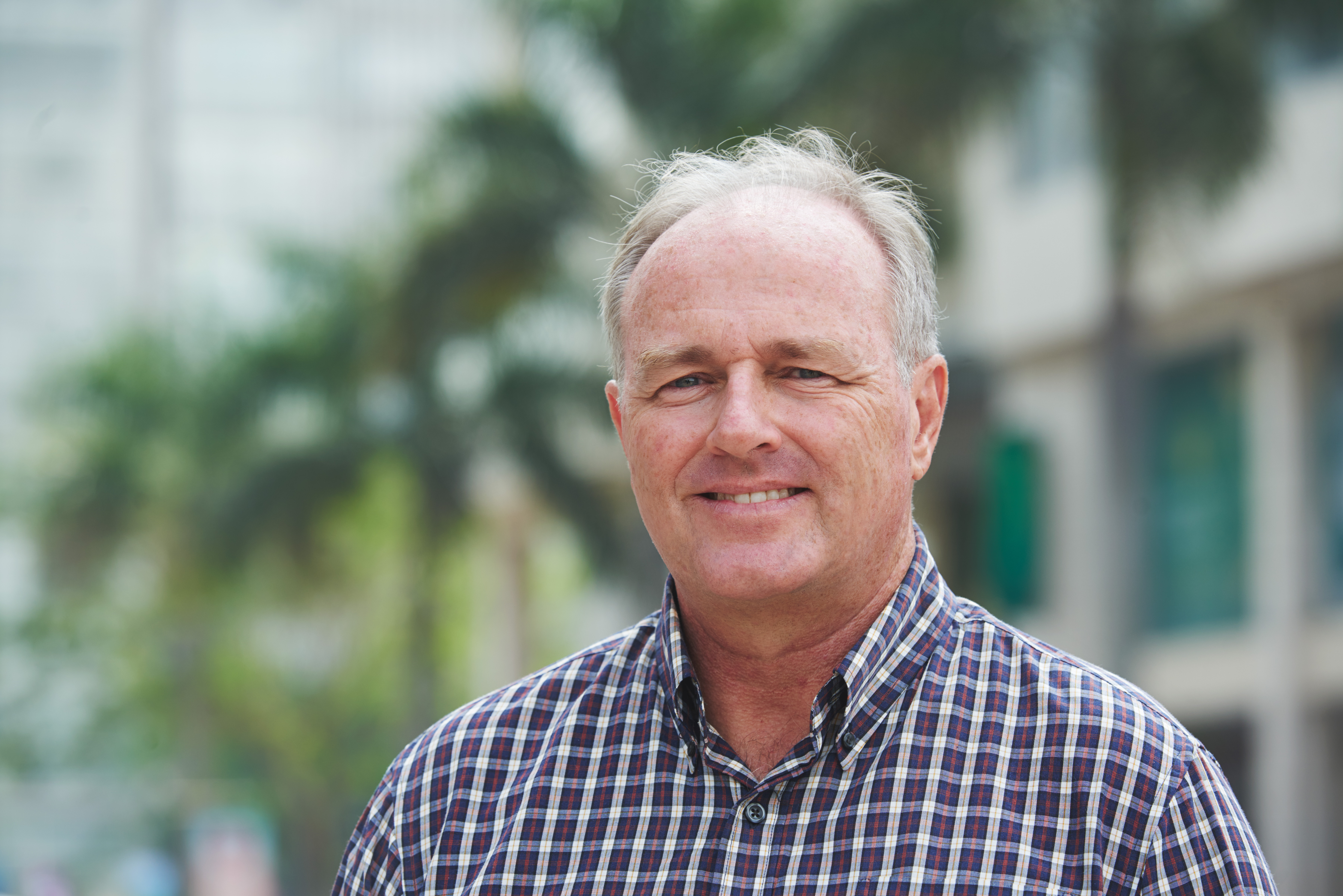 A person outside in a city wearing a checkered button-up shirt smiling.