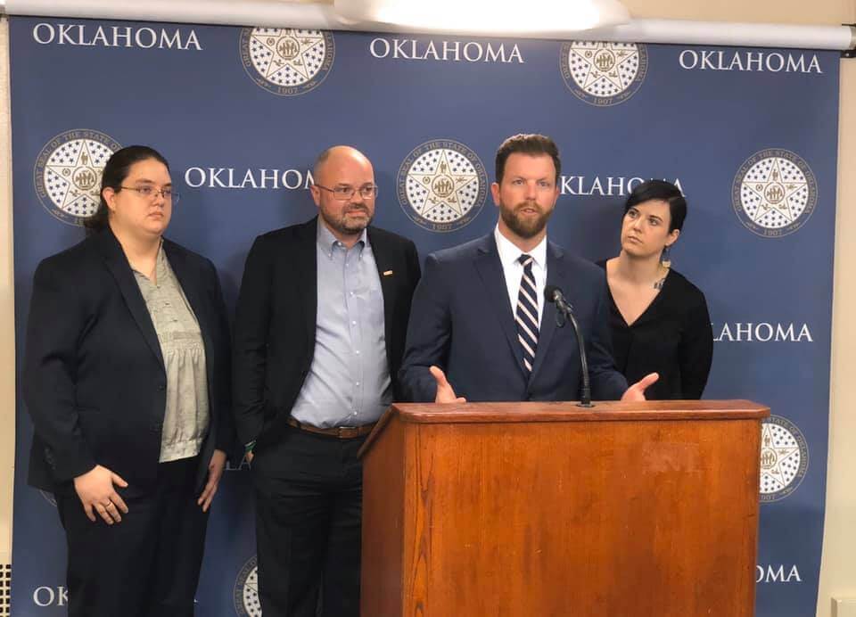 Three people stand behind Representative Jason Dunnington as he speaks at a podium.