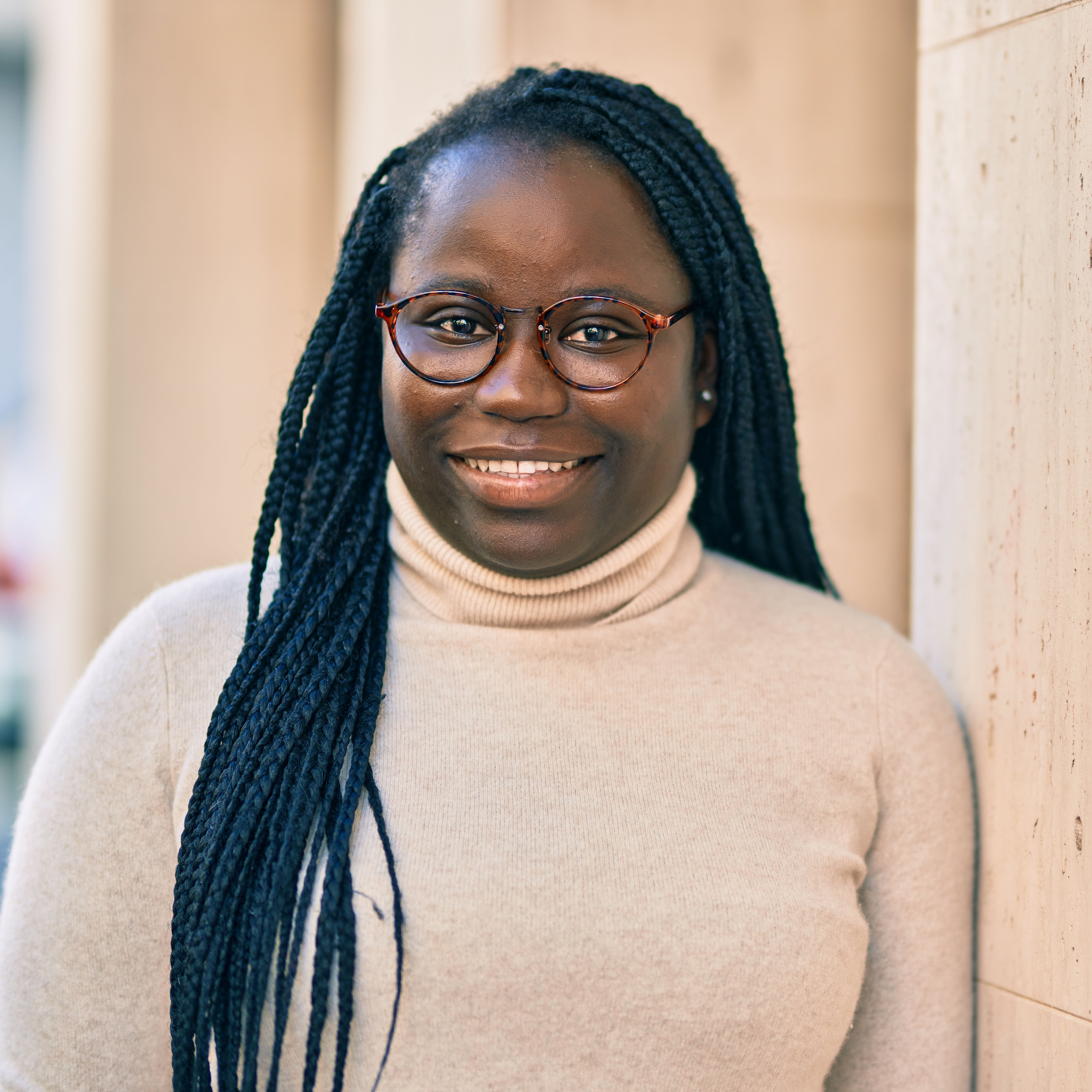 A person wearing glasses leaning against a stonewall smiling.