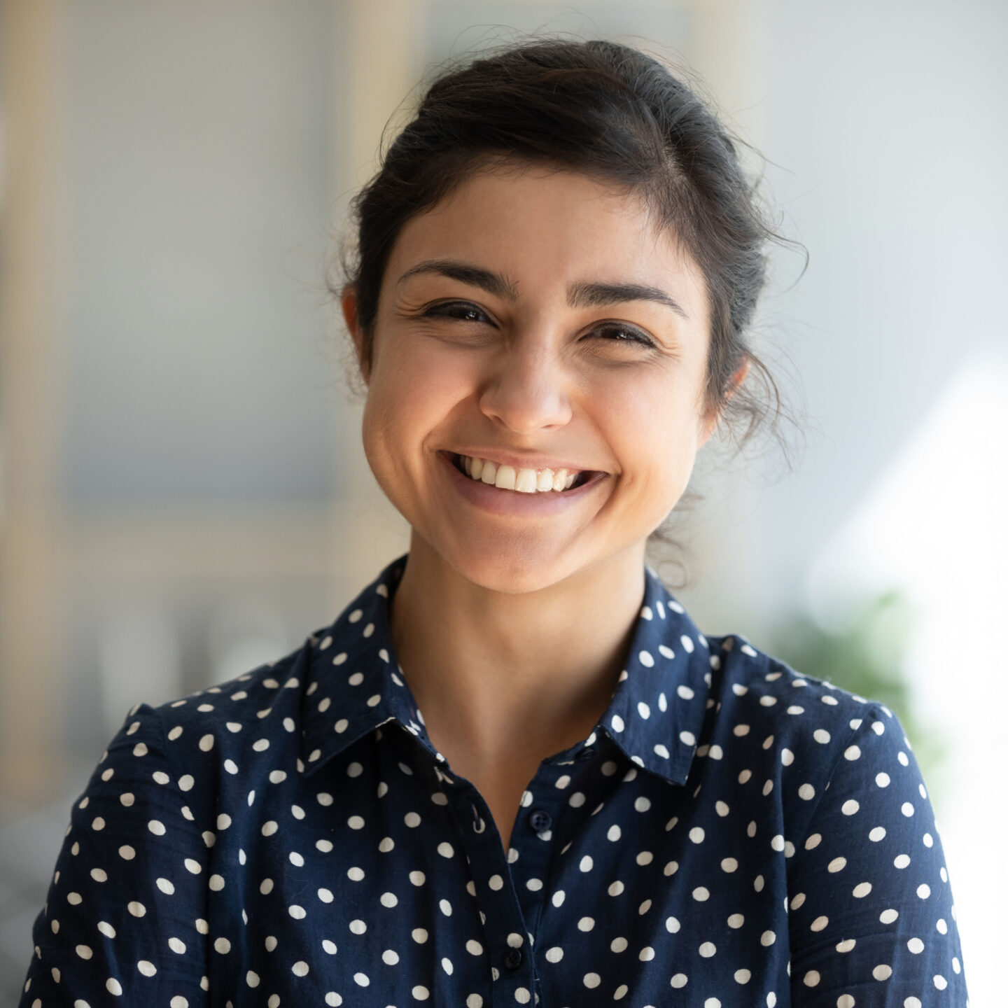 A person in a blue and white polka-dotted shirt smiling in their home.