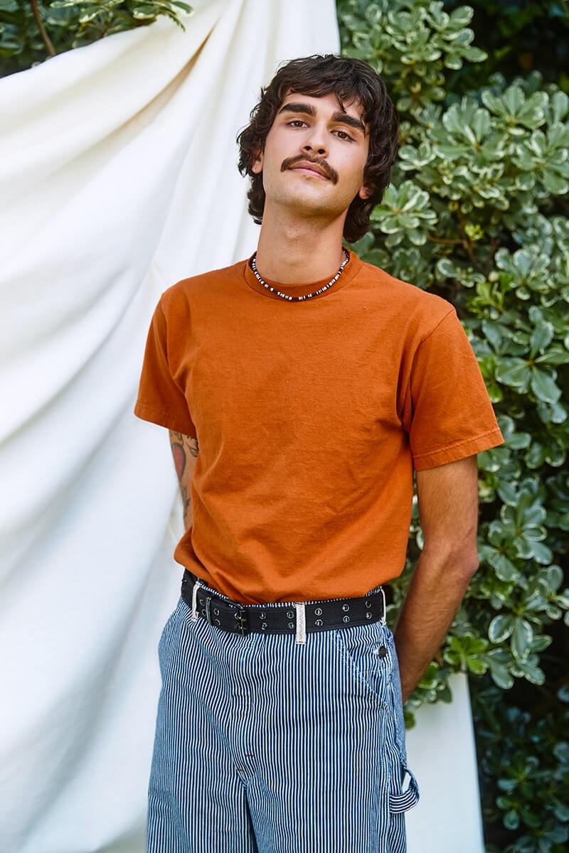 Portrait of a LGBTQ young person wearing an orange shirt with a white backdrop