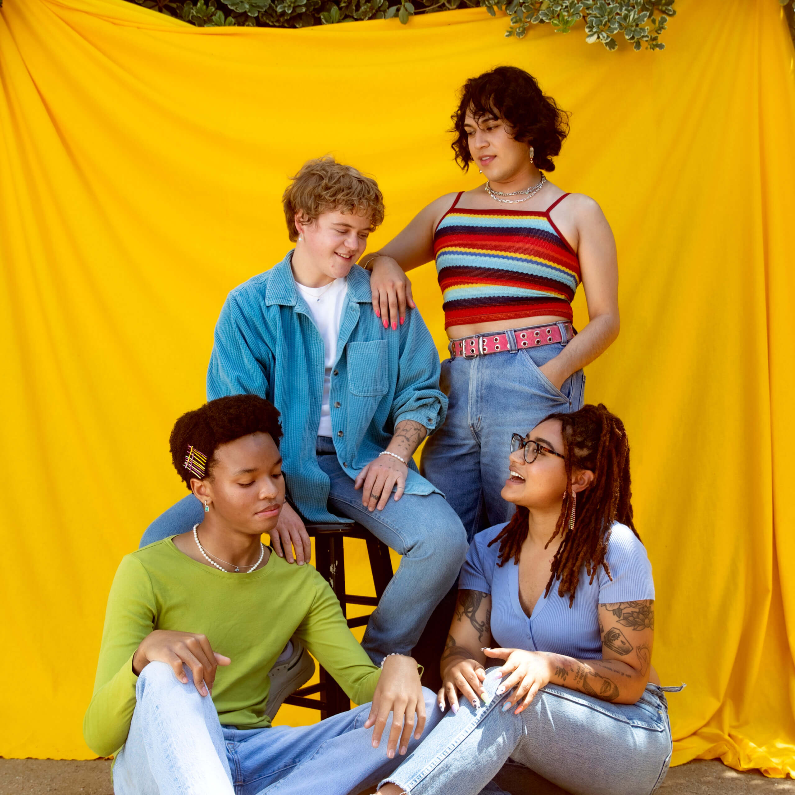 Four young people in colorful clothing standing against a yellow backdrop talking.