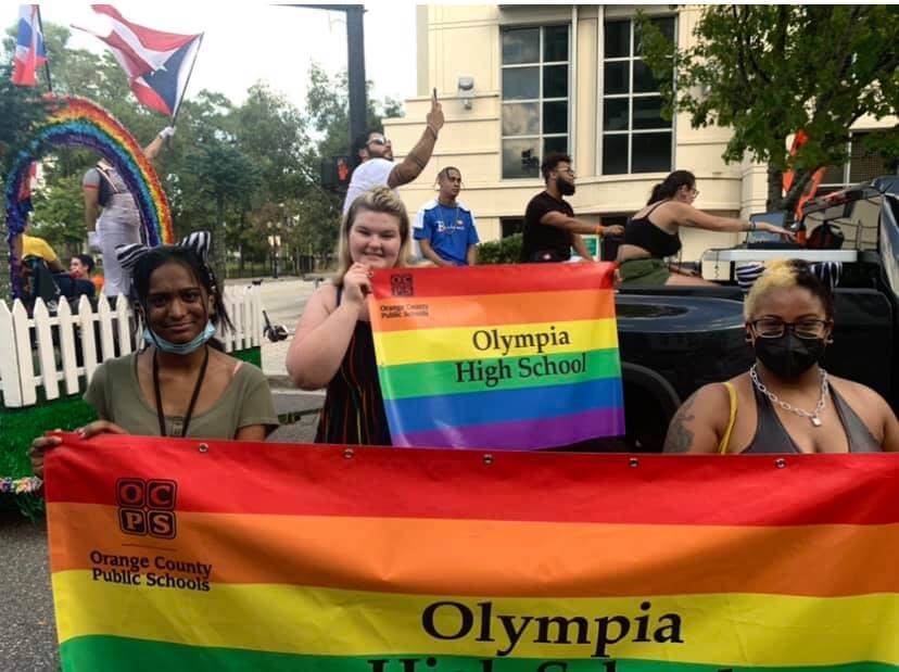 People at a Pride Parade carrying a rainbow colored banner that reads Olympia High School