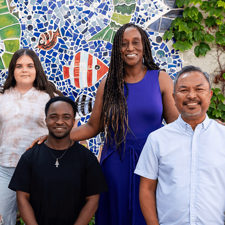 A group of people standing and sitting in front of a mosaic background.