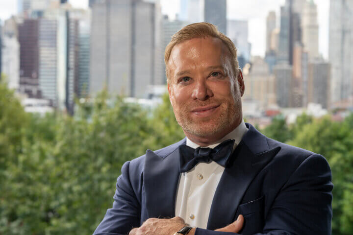 A smiling Jim DeCarlo-Schnepper in front of a city background.