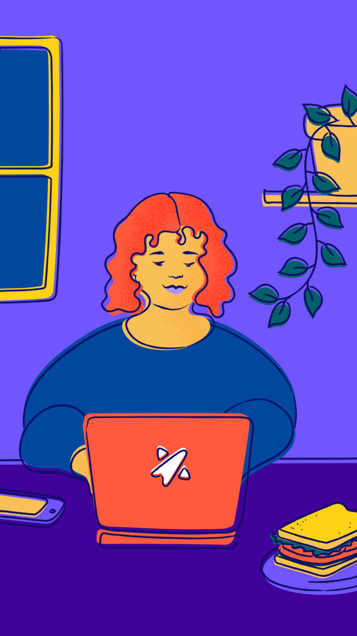 Smiling young female-presenting person sitting at a desk working on a computer.